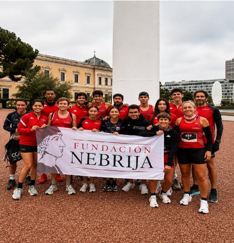 Un grupo de atletas posando frente a un monumento con una bandera de la Fundación Nebrija.