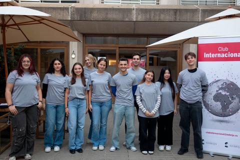 Un grupo de jóvenes con camisetas grises posa frente a un cartel del Club Internacional.
