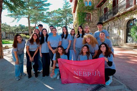Grupo de personas sonrientes posando al aire libre con una bandera de la Fundación Nebrija.