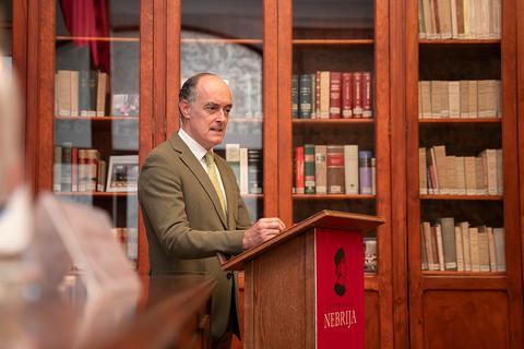 Un hombre de pie frente a un podio en una biblioteca con estanterías llenas de libros.