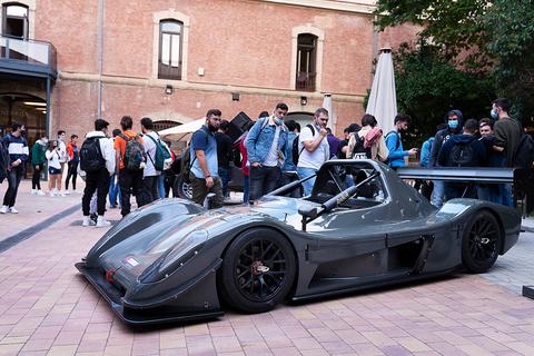 Un coche de carreras deportivo se encuentra estacionado mientras un grupo de personas lo observa.