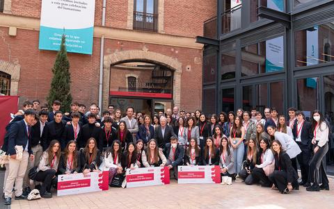 Un grupo de jóvenes se reúne frente a un edificio, todos vestidos con distintivos y sonriendo para la foto.