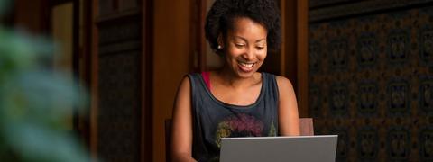 Una mujer sonriente trabaja en su laptop en un ambiente acogedor.