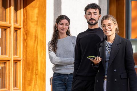 Tres personas posan frente a una pared de madera, cada una con una expresión amigable.