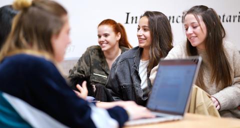 Un grupo de cuatro jóvenes sonríen y conversan en un entorno informal, mientras una de ellas está frente a un portátil.
