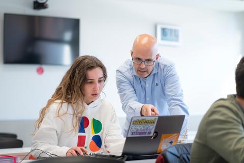 Un profesor ayuda a una estudiante mientras trabaja en su computadora portátil.