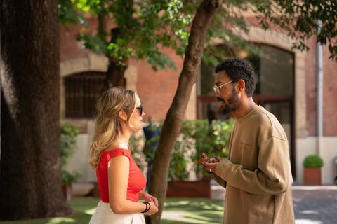 Una pareja de personas conversando en un entorno al aire libre con árboles y plantas.