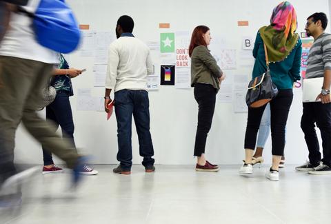 Un grupo de personas observa y discute carteles en una pared durante un evento o exposición.
