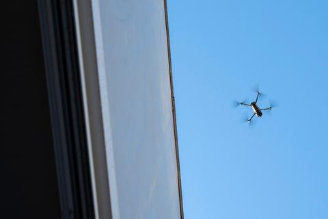 Un dron vuela sobre un edificio bajo un cielo azul.