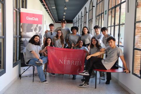 Un grupo de estudiantes posando junto a una pancarta de la Fundación Nebrija en un pasillo con ventanas.