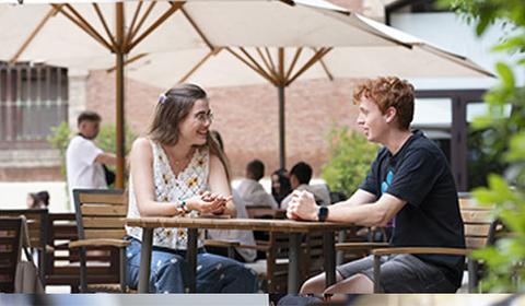 Dos personas conversando en una terraza al aire libre.