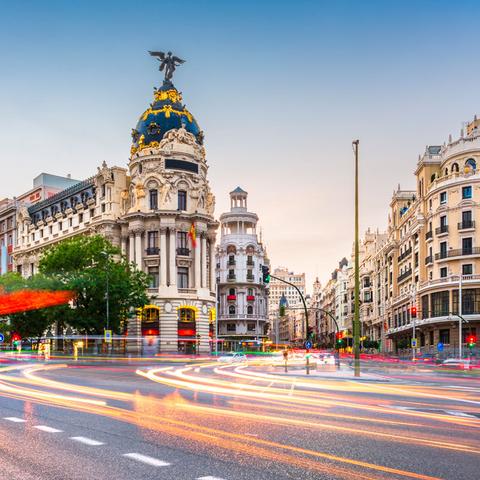 La imagen muestra una intersección en una ciudad con arquitectura histórica y moderna al fondo.