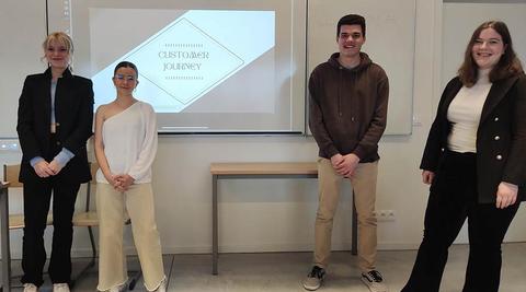 Un grupo de cuatro estudiantes se presenta frente a una pantalla con una diapositiva sobre el 'Customer Journey'.